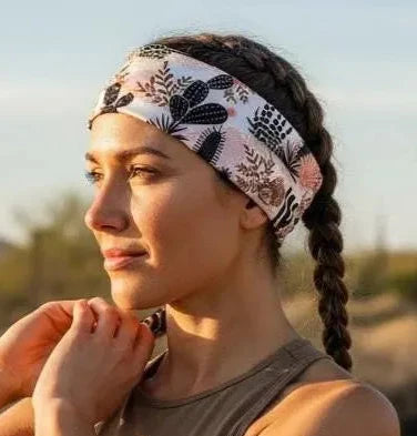 A woman outdoors in a desert setting wearing a patterned athletic headband and a brown sports tank top, with her hair in a side braid.