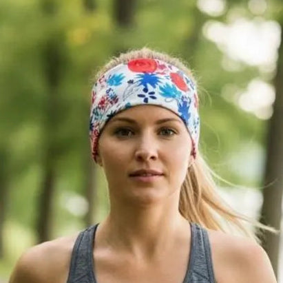 A woman jogging outdoors on a tree-lined path, wearing a white athletic headband with a colorful red, blue, and green floral pattern and a gray tank top.