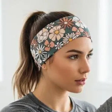 A woman in a gym wearing a gray long-sleeve athletic top and a floral patterned headband, posing with one arm raised.