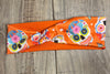 Sugar Skull with pink blue yellow and orange flowers on an orange background with moisture wicking underneath