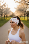 Woman running outdoors wearing a white tank top and cherry-patterned headband.