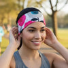 A woman in a gray athletic tank top wearing a colorful floral-patterned headband, adjusting it in an outdoor park setting.