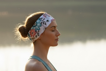 Woman meditating on a wooden deck by a lake at sunset