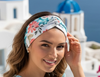 Woman in a light blue dress with a floral headband sitting on a rooftop with a scenic view of Santorini.