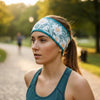 A woman wearing a floral athletic headband with teal trim, photographed outdoors on a park path during warm golden-hour light.