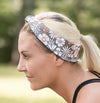 Blonde woman wearing floral workout headband and black sports top exercising outdoors on grass