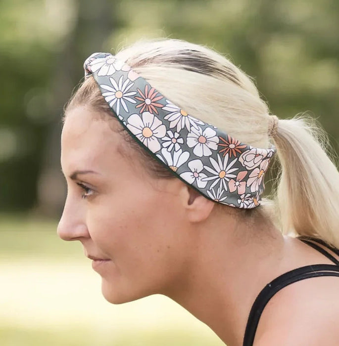 Blonde woman wearing floral workout headband and black sports top exercising outdoors on grass