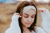 Woman wearing a white handmade workout headband and a white knitted sweater outdoors with a blurred natural background