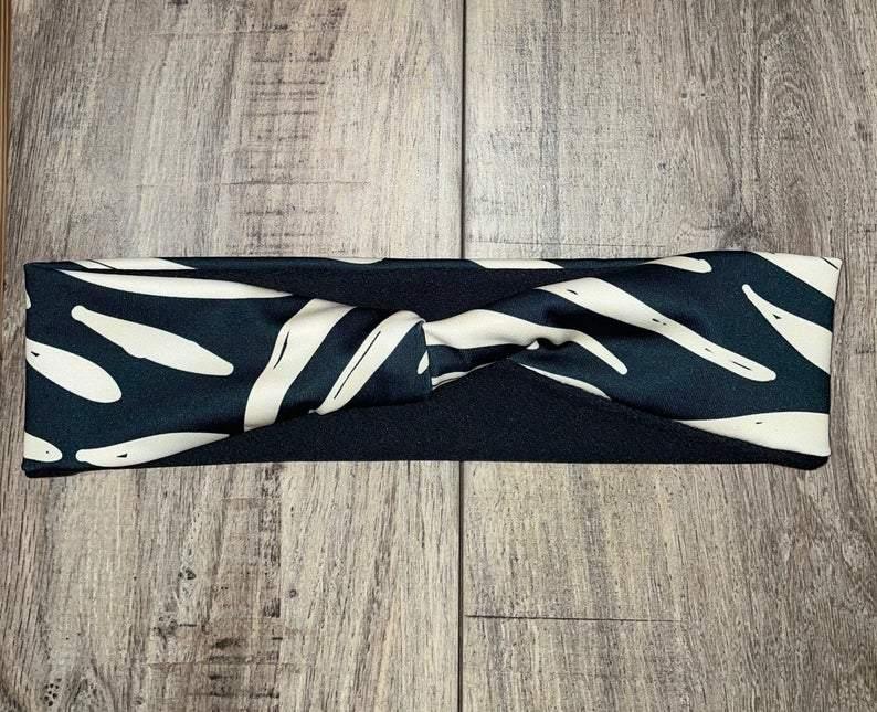 Handmade black and white patterned workout headband twisted at center on wood floor moisture wicking material underneath