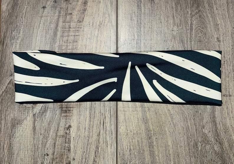 Black and white handmade workout headband with an abstract leaf pattern, displayed on wooden surface
