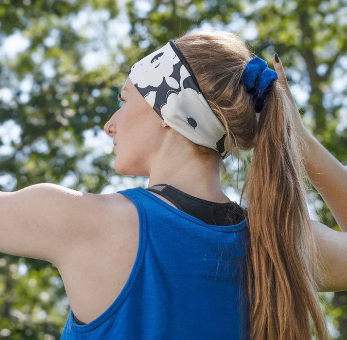 Woman wearing black and white floral workout headband and blue tank top with blue scrunchie outdoors