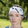 Woman wearing black and white floral workout headband and blue tank top outdoors with green trees in background