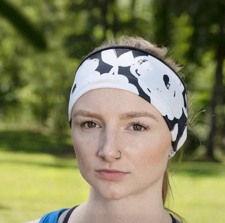 Woman wearing black and white floral workout headband and blue tank top outdoors with green trees in background