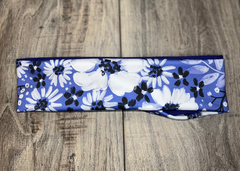 Handmade workout headband with white and black floral pattern on blue background, placed on wooden floor