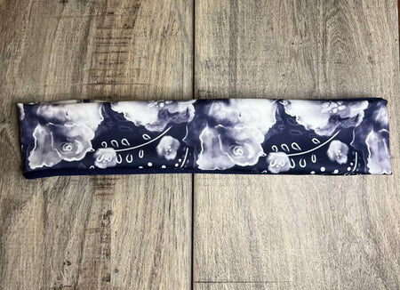 Handmade navy blue workout headband with white and light purple floral pattern on wooden surface