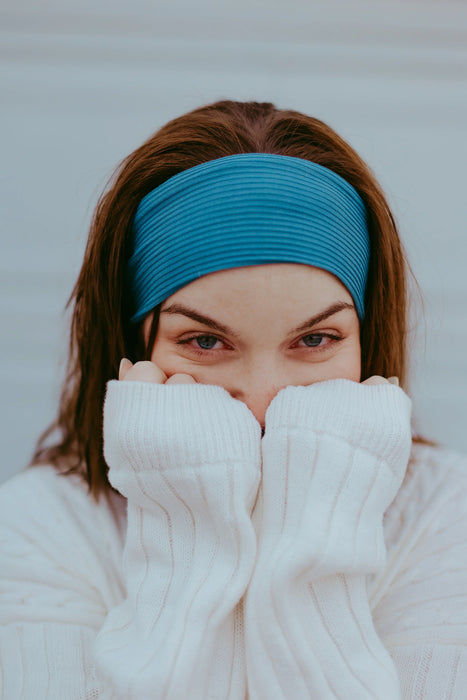 Woman wearing a blue workout headband and cozy white sweater covering her face, close-up