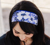 Woman wearing a blue and white floral workout headband with black long sleeve top, sitting on white wooden floor
