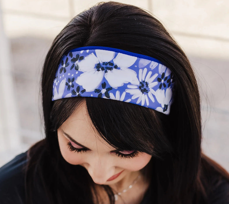 Woman wearing a blue and white floral workout headband with black long sleeve top, sitting on white wooden floor