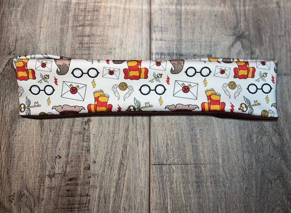 Athena Fitness Collections white workout headband with witch inspired print featuring glasses, letters, keys, scarves, and magical symbols on wood background