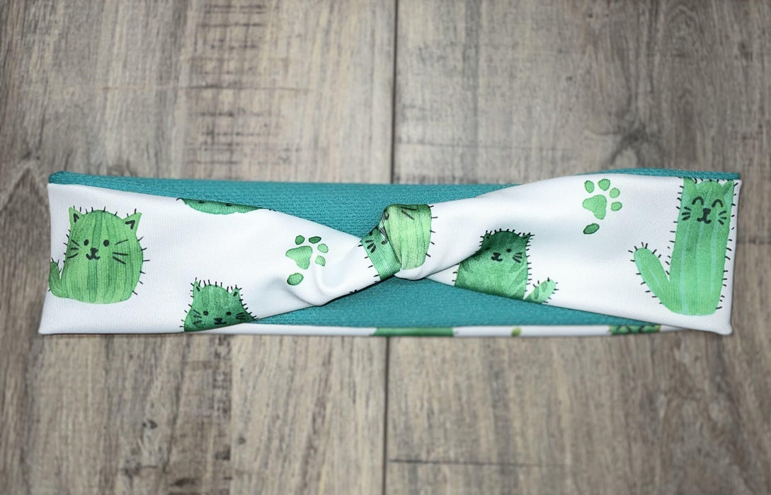 Athena Fitness handmade workout headband with green cactus cat prints and teal fabric on wooden background