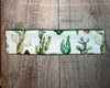 Handmade workout headband with green cactus print and sun design laid on wooden surface