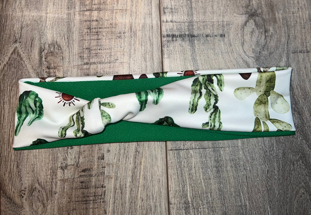Handmade workout headband with cactus print pattern on white fabric and solid green back, laid flat on wooden surface