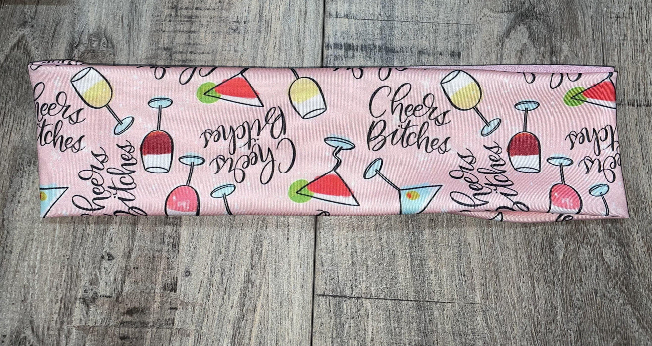 Pink workout headband with Cheers Bitches text and colorful cocktail glass illustrations on wood floor