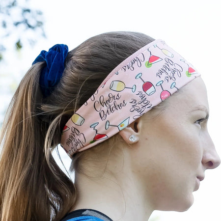 Side profile of woman wearing pink workout headband with colorful drinks pattern and text, blue tank top outdoors