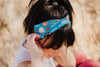 Woman wearing a blue workout headband with coffee-themed designs and text outdoors