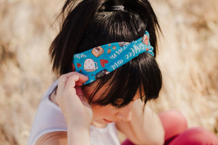 Woman wearing a blue workout headband with coffee-themed designs and text outdoors