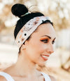 Smiling woman in white tank top wearing a patterned workout headband with trees in soft-focus background