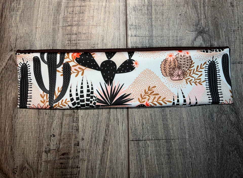 Handmade nonslip workout headband with black and brown cactus print on white fabric, laid on wooden surface