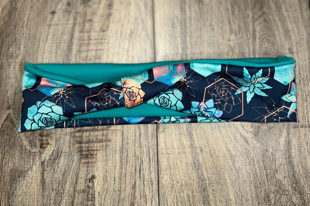 Handmade teal workout headband with floral and geometric pattern on wooden floor