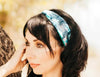 Woman wearing a blue floral workout headband, standing outdoors beside a tree, showcasing Athena Fitness style