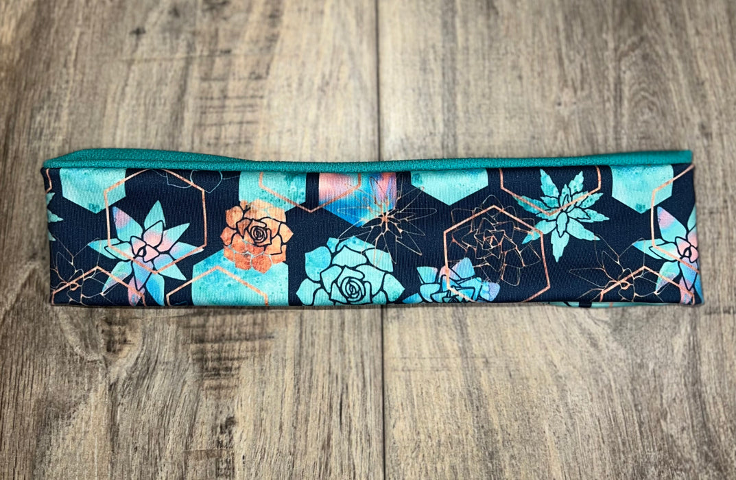 Athena Fitness moisture wicking workout headband with blue and orange succulent floral pattern on wooden surface