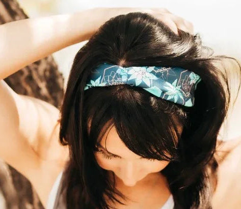 Woman wearing a blue floral moisture wicking workout headband and gray tank top outdoors near a tree