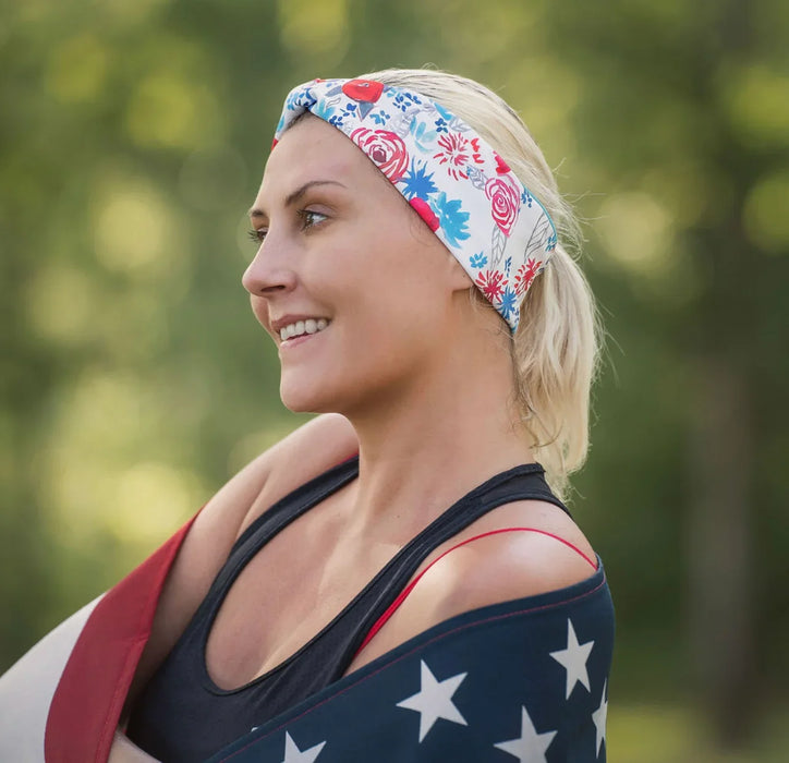 Smiling woman wearing a floral workout headband and black tank top, wrapped in a star-spangled American flag outdoors