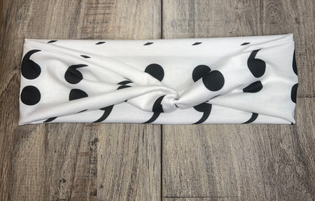 White workout headband with black semicolon pattern, knotted center on rustic wood background