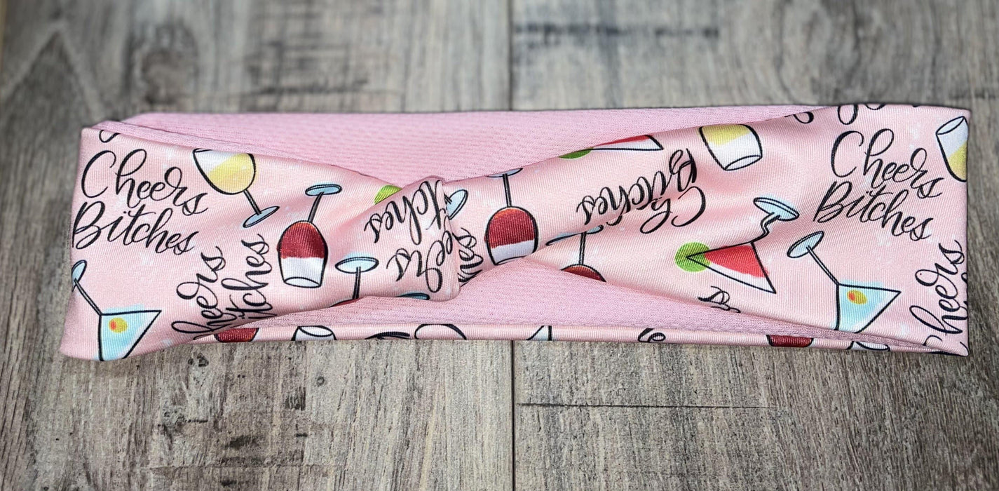 Pink workout headband with colorful cocktail glass prints and Cheers Bitches text on wooden surface
