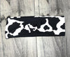 Black and white cow print workout headband with twisted knot design on wooden floor