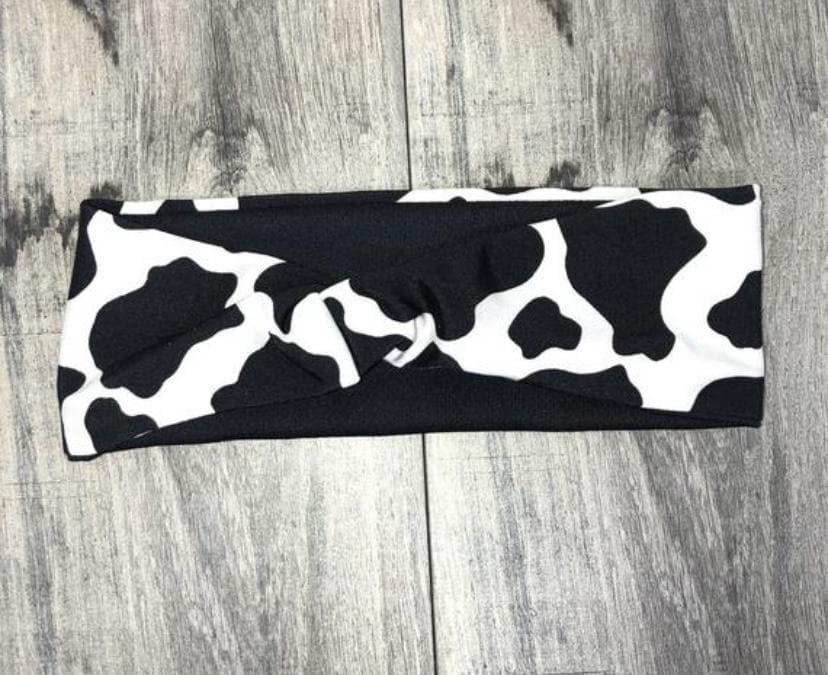 Black and white cow print workout headband with twisted knot design on wooden floor