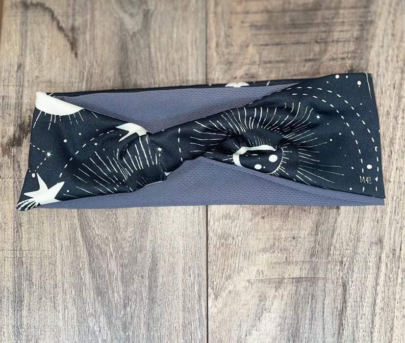 Black and gray workout headband with white celestial star and sunburst pattern on wooden background