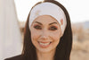 Smiling woman with long dark hair wearing a white handmade workout headband outdoors in desert setting