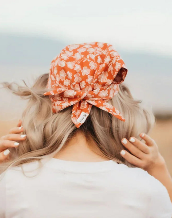 Woman in white t-shirt and high-waisted jeans wearing an orange floral workout hair scarf outdoors on a dirt path