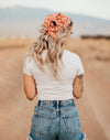 Woman with long blonde hair wearing an orange floral workout hair scarf, white t-shirt, and denim shorts outdoors