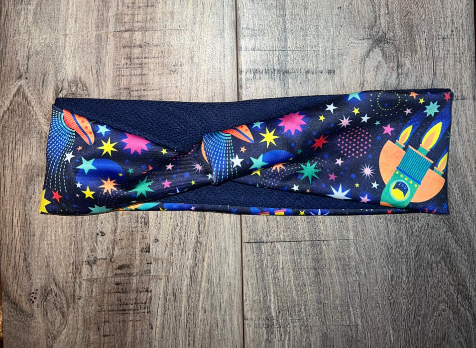 Athena Fitness colorful workout headband with star, planet, and rocket patterns on wooden surface