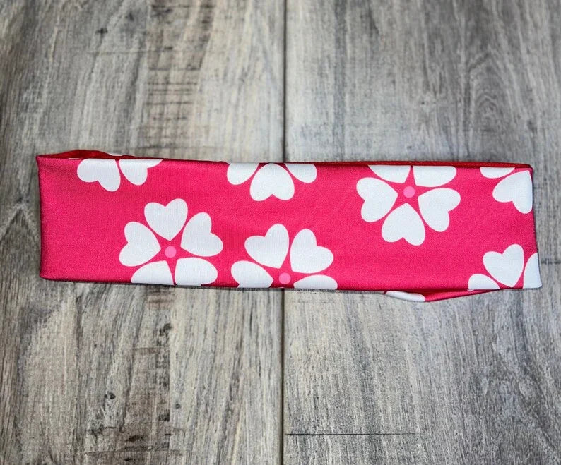 Pink workout headband with white heart-shaped flower patterns on wooden surface, Athena Fitness Collections