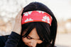 Woman wearing a pink workout headband with white heart patterns outdoors, dressed in black long-sleeve top