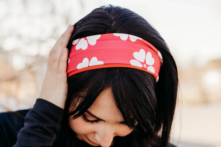 Woman wearing a pink workout headband with white heart patterns outdoors, dressed in black long-sleeve top