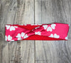 Pink workout headband with white flower pattern, laid flat on wood background, Athena Fitness Collections